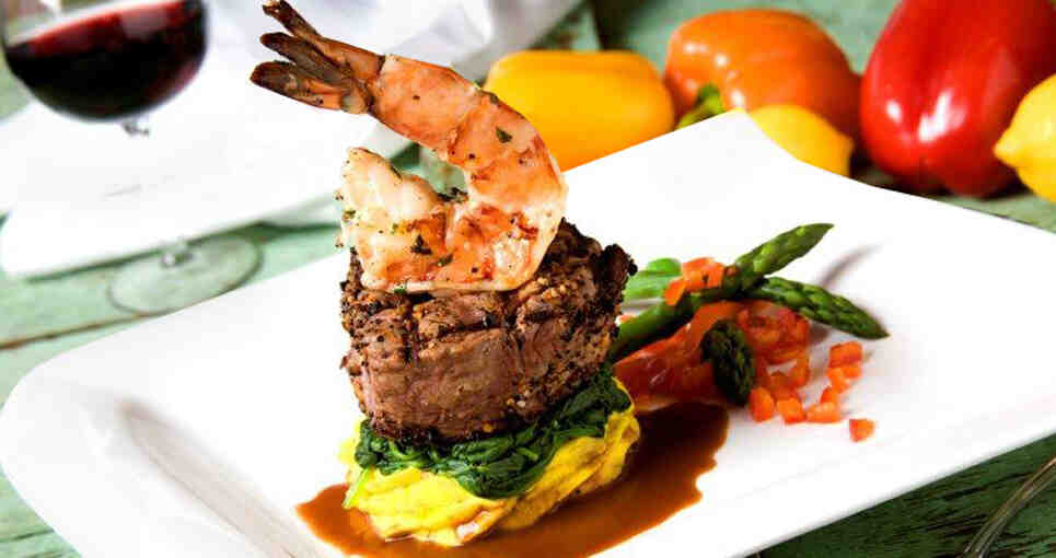 Gourmet filet mignon topped with succulent shrimp, served with fresh vegetables on a white plate.
