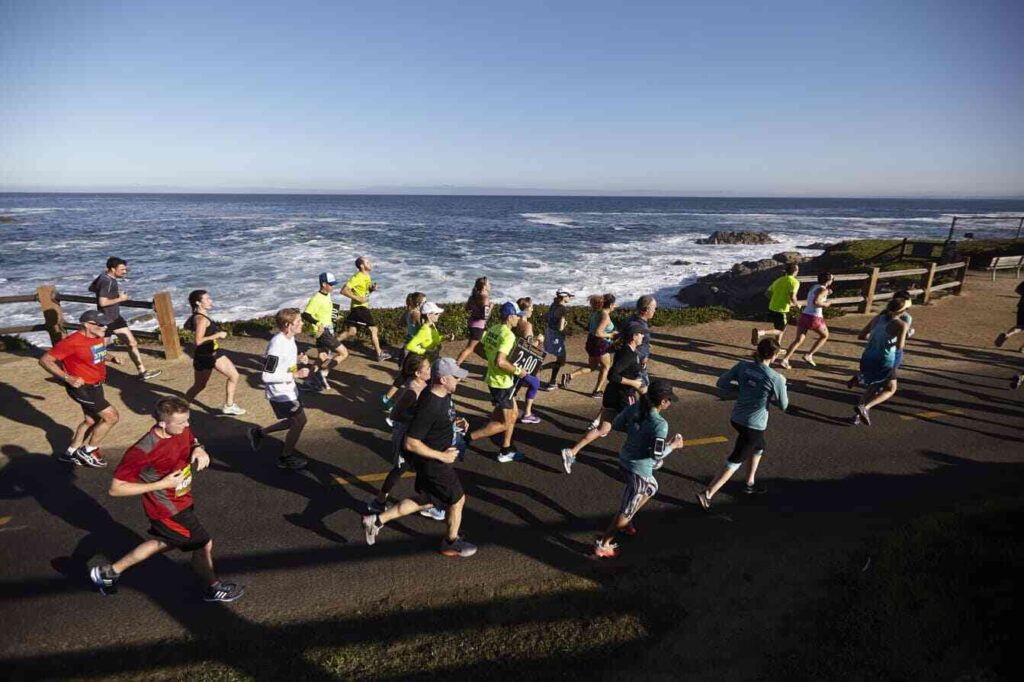 Runners stretching and preparing under the bright sun before the start of the Monterey Bay Half Marathon.