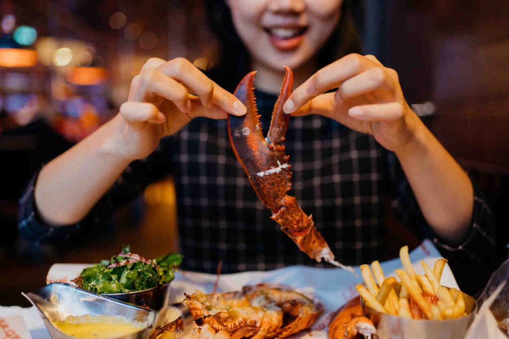 an Asian Chinese woman holding lobster claw and having a grilled lobster meal in Whaling Station Steakhouse