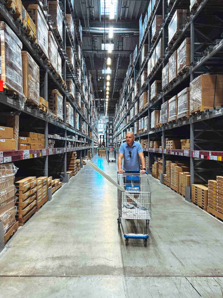 Mature man standing with trolley cart in huge distribution warehouse