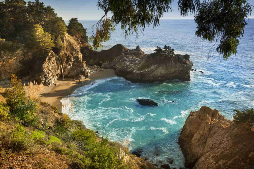 McWay Falls cascading into a turquoise cove surrounded by rugged cliffs at Julia Pfeiffer Burns State Park in Big Sur.